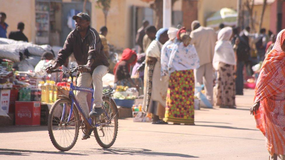 A man on a bicycle riding past a street market in Asmara, Eritrea