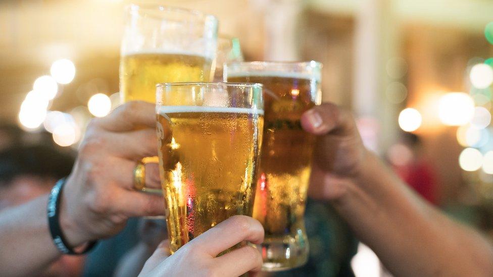 Close up of three hands pushing glasses of beer together in a cheers style