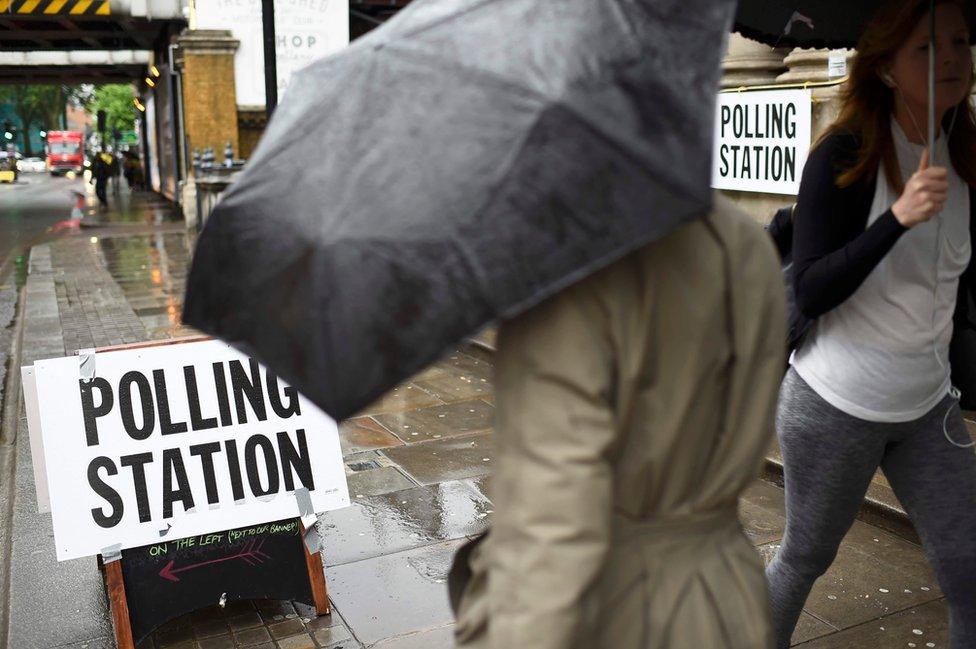 Pedestrians carrying umbrellas during heavy rainfall pass a polling station, on the day of the EU referendum, in central London