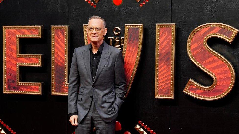 Tom Hanks in front of large Elvis sign