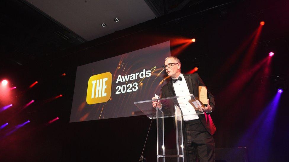 Anglia Ruskin's vice chancellor Roderick Watkins making a speech on stage having scooped the award under his arm