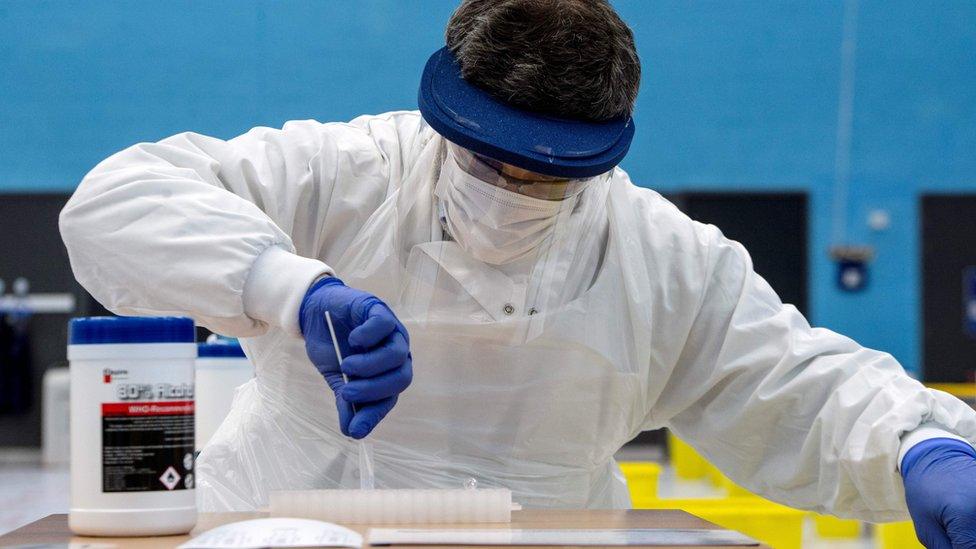 A third-year medical student from the University of St. Andrews, wearing full PPE, completes a fellow student's lateral-flow COVID-19 test in a mass testing centre set up in the University's sports hall in St. Andrews