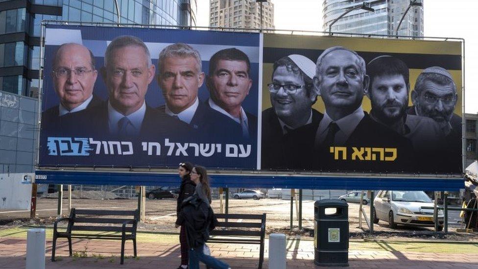 Israelis walk past billboards put up by the centrist Israeli Blue and White alliance parties featuring their candidate for Prime Minister, Benny Gantz, alongside a panel showing the Likud party (R) with Prime Minister Benjamin Netanyahu and extreme right-wing members of the Likud party, in Tel Aviv's diamond district, 15 March 2019