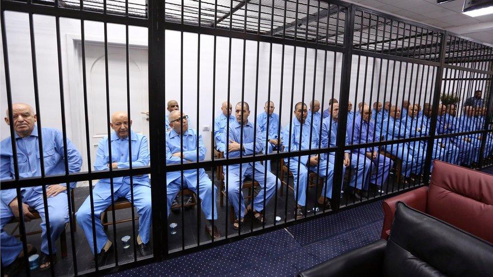 Gaddafi's former aides sit dressed in prison blue behind the bars of the accused cell during their trial at court of appeals in the Libyan capital, Tripoli.