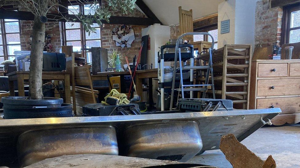 The inside of Krumbz cafe with the flooring removed, a sink and debris resting on the floor and multiple furniture units piled up in the middle of the cafe floor