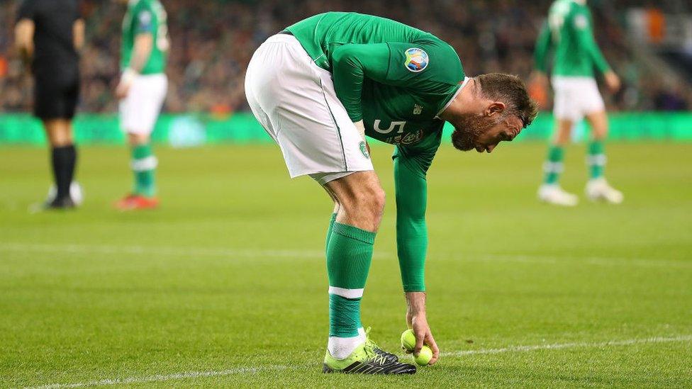 Richard Keogh of Ireland removes tennis balls thrown on to the pitch.