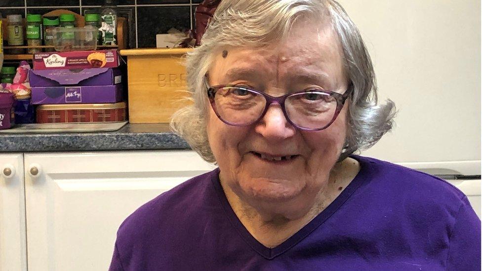 Joan Narey is 90 and wearing glasses and wearing a purple top