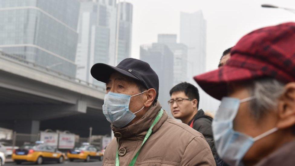 People wear masks while waiting for a bus on a polluted day in Beijing on February 27, 2018