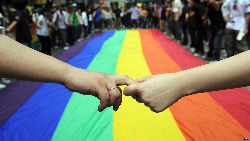 People holding hands in a human chain around a rainbow flag