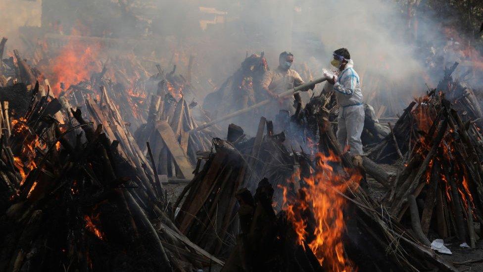 Relatives stand next to the burning funeral pyres of those who died due to the coronavirus disease (COVID-19), at Ghazipur cremation ground in New Delhi.