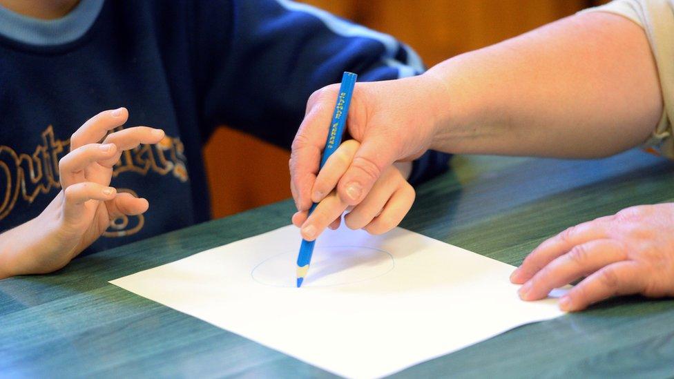 woman helping child with learning disability use a pencil