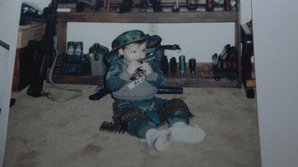 A photograph of a toddler sitting surrounded with weapons