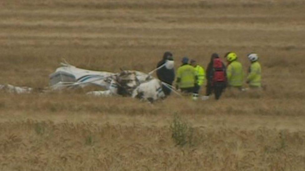 The crash plane in the field with emergency personnel around it