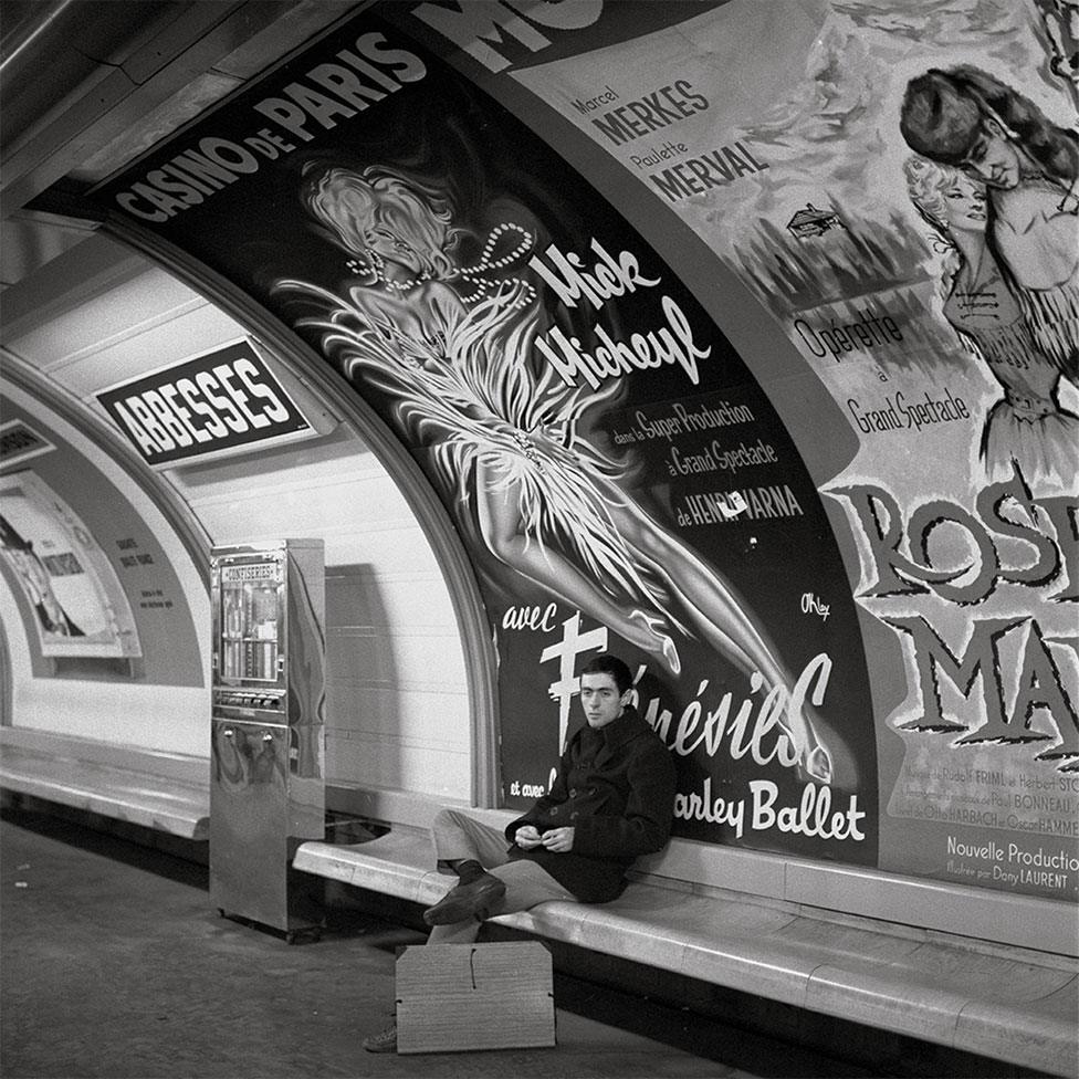 A man sits and waits on a Metro platform with a giant poster behind him