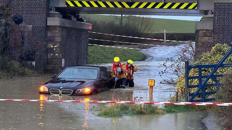 Firefighters rescuing man from car in flood water