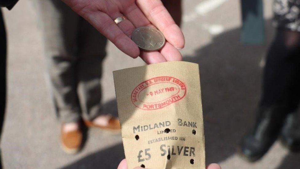 a small brown bag and a hand holding a silver coin