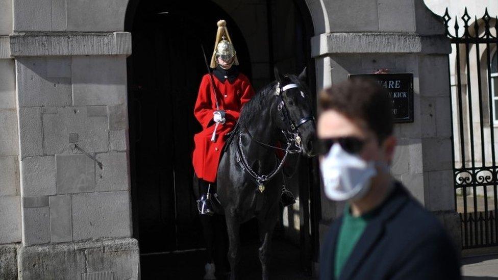 A man wearing a protective face mask walks past a member of the household cavalry on Whitehall