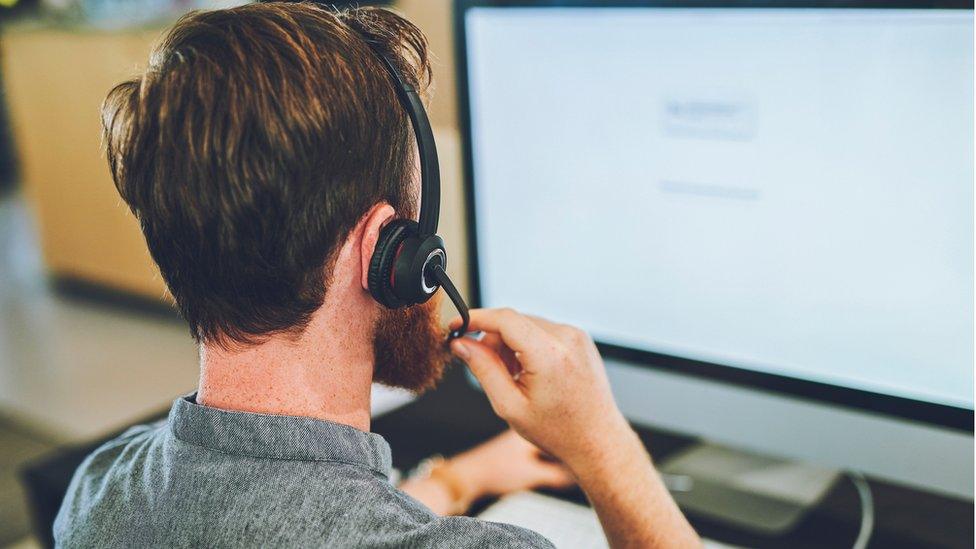 Man talking on a headset while working or assisting on computer screen in a office.