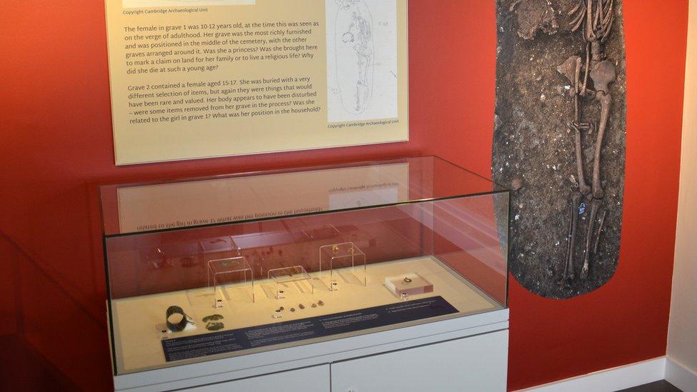 A glass display case containing amethyst beads, a metal workbox, a broken brooch and other grave goods