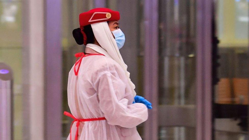 Am airline staffer (In July) wearing protective gear looks on as tourists get a medical screening upon arrival at Terminal 3 at Dubai airport, in the United Arab Emirates