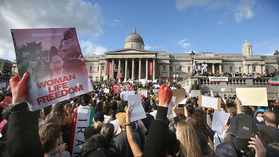 Protesters in Trafalgar Square holding up Iranian flags and photos of Mahsa Amini