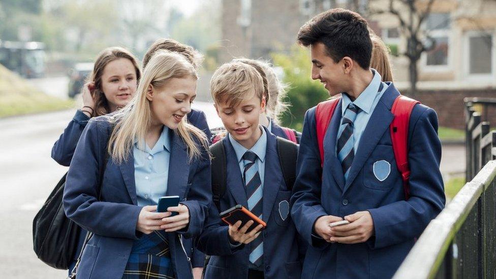 Children in uniform looking at mobile phones