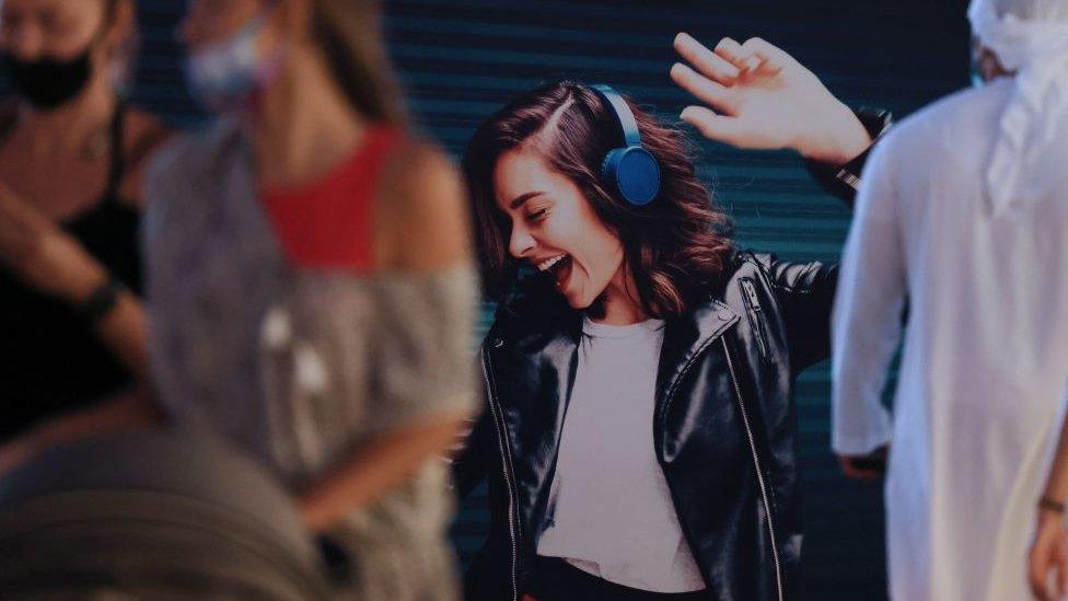 Women walk past a poster of a dancing woman with headphones on, near Jumeirah Beach in Dubai