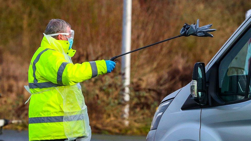 An NHS Test and Trace worker hands a person a test kit in a drive through testing centre in Southport