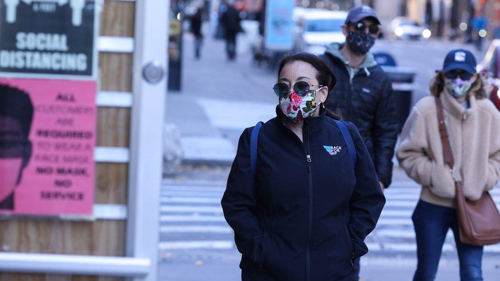 Pedestrians walk past a store with guidelines for social distance and face masks