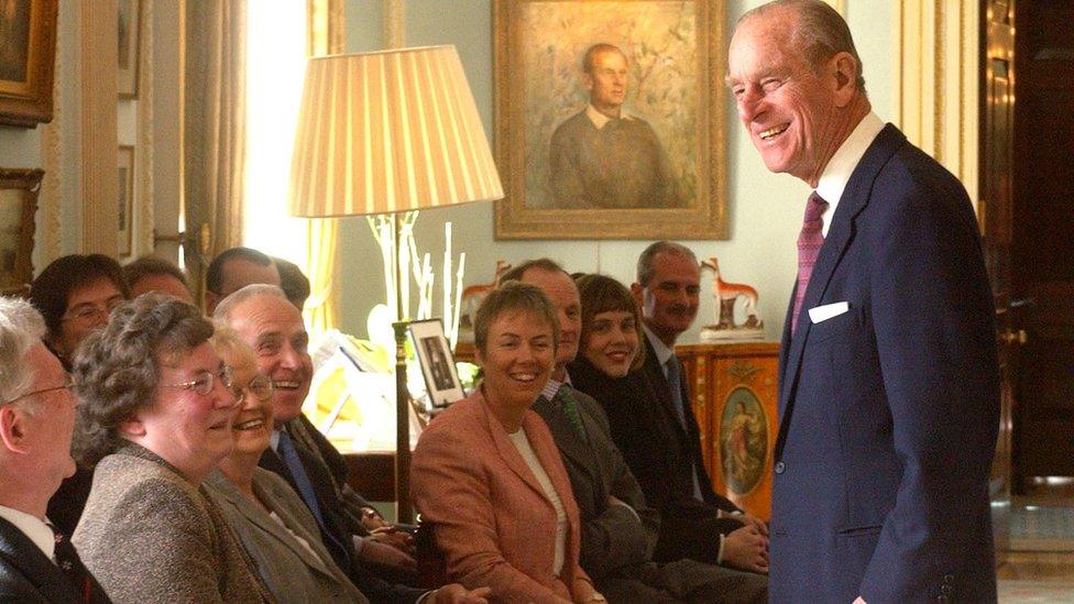 A portrait of a youthful Prince Philip hangs on the wall in Hillsborough Castle as he shares a joke with parents of Duke of Edinburgh gold award winners in February 2004