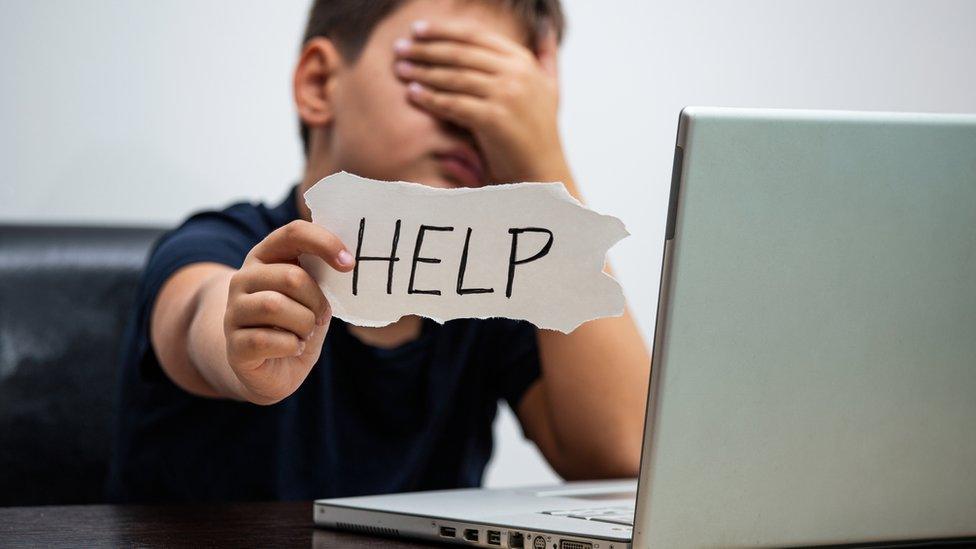 Boy holds up help sign next to computer