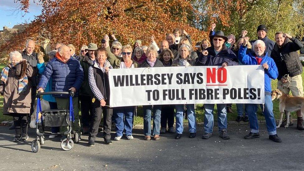 A group of people holding a banner saying Willersey Says No To Full Fibre Poles