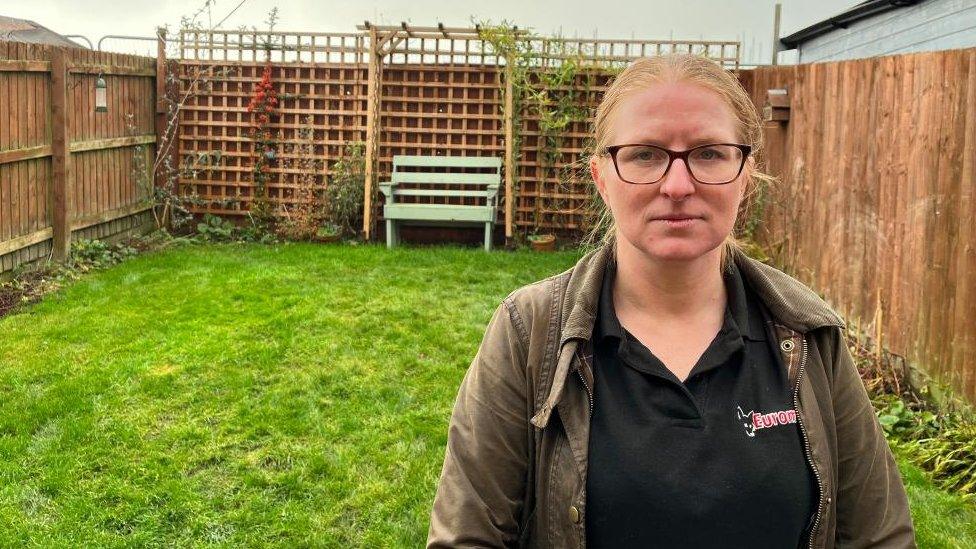 Garden with high wooden fences. A woman with short brown hair and glasses in the foreground.