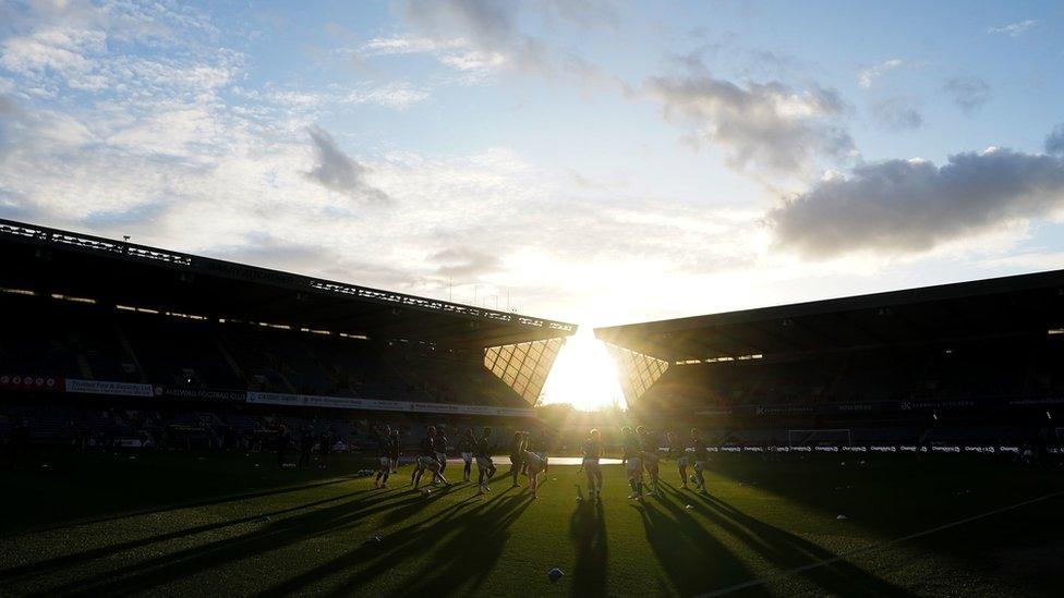 A general view inside of the New Den with the sun shining through onto the pitch where players warm up