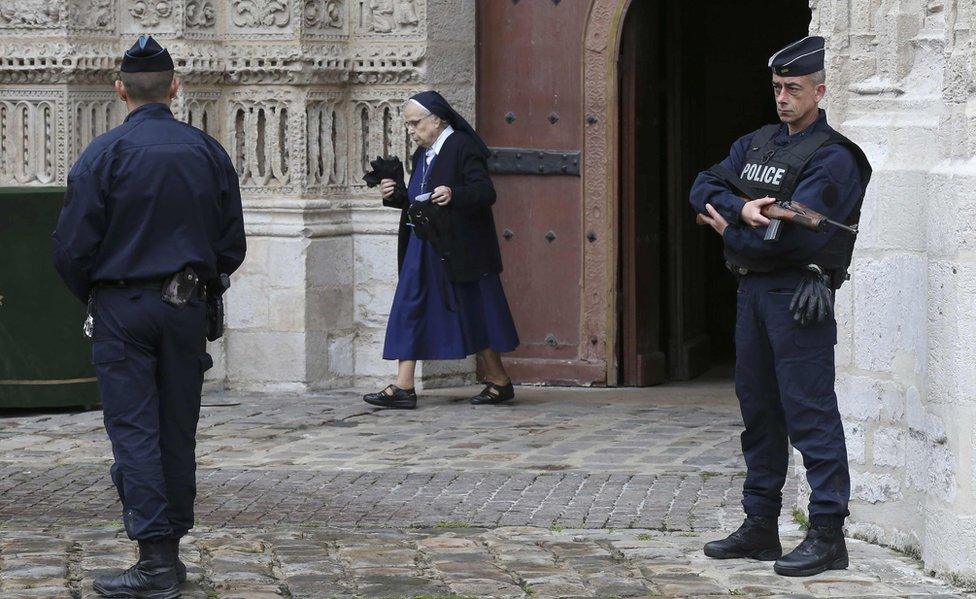 Two French policemen on guard outside a cathedral as a nun walks out