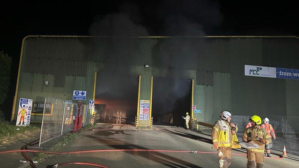 Smoke billows out of the open doors as firefighter congregate outside the building