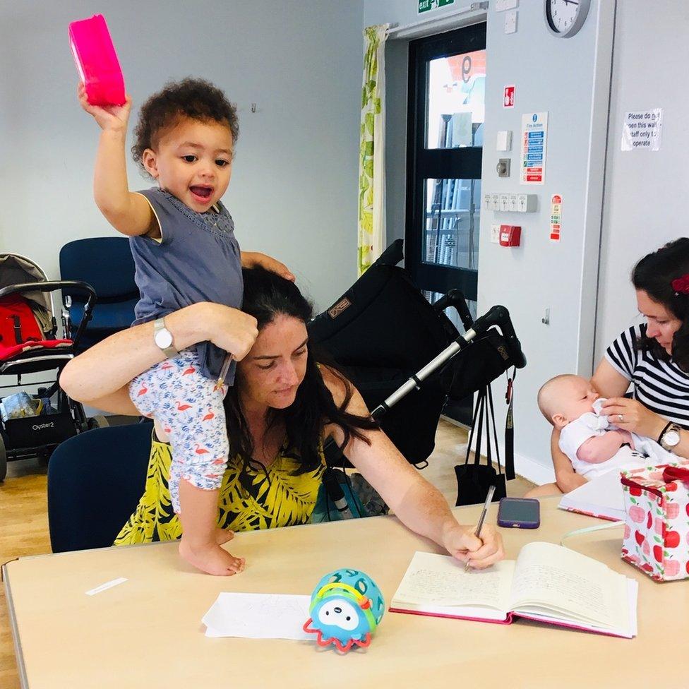 Baby standing on table as woman tries to write