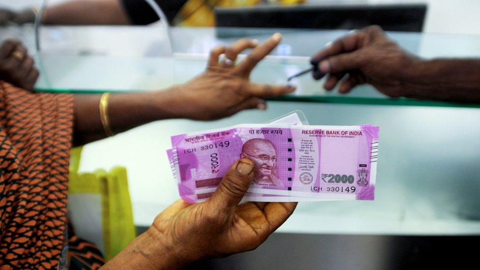 An Indian woman holds 2000 INR notes as she has her finger marked with indelible ink after exchanging 500 and 1000 INR banknotes at a bank in Chennai.