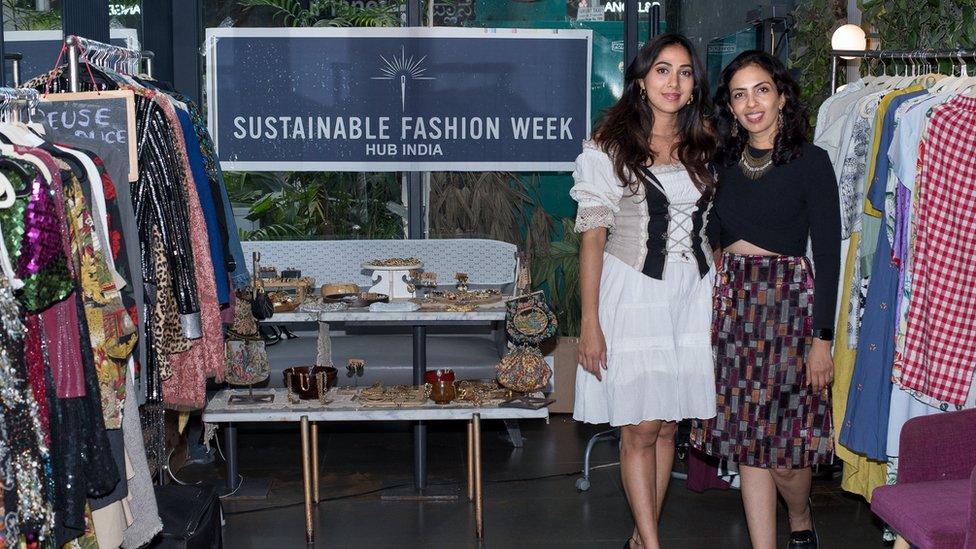 Priyanka Abhishek and Laghna Gowda standing near clothes rails by a Sustainable Fashion Week sign