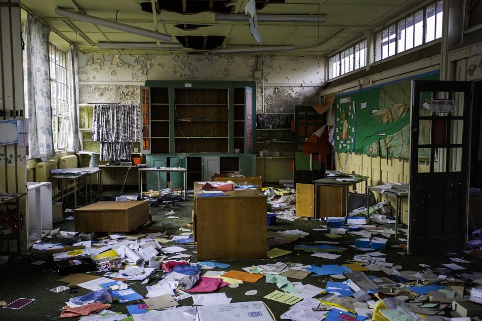 A derelict classroom with papers on the floor