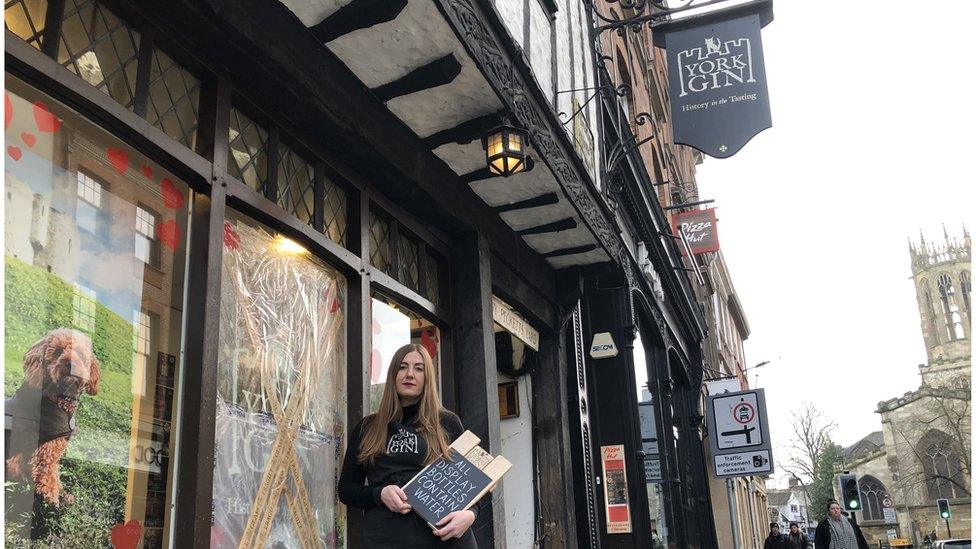 Shop worker stands in front of broken store window