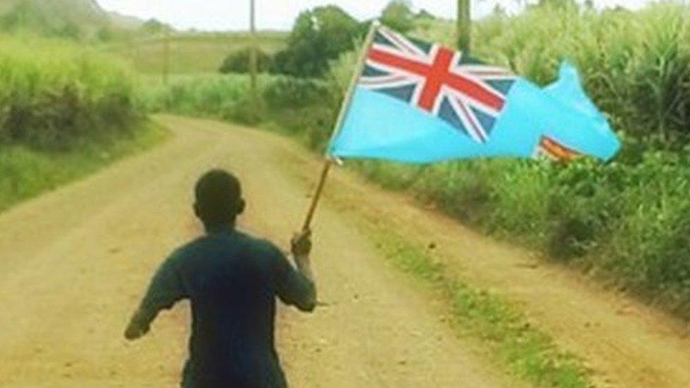 A Fiji boy runs down a dirt road, cheering on the rugby sevens team