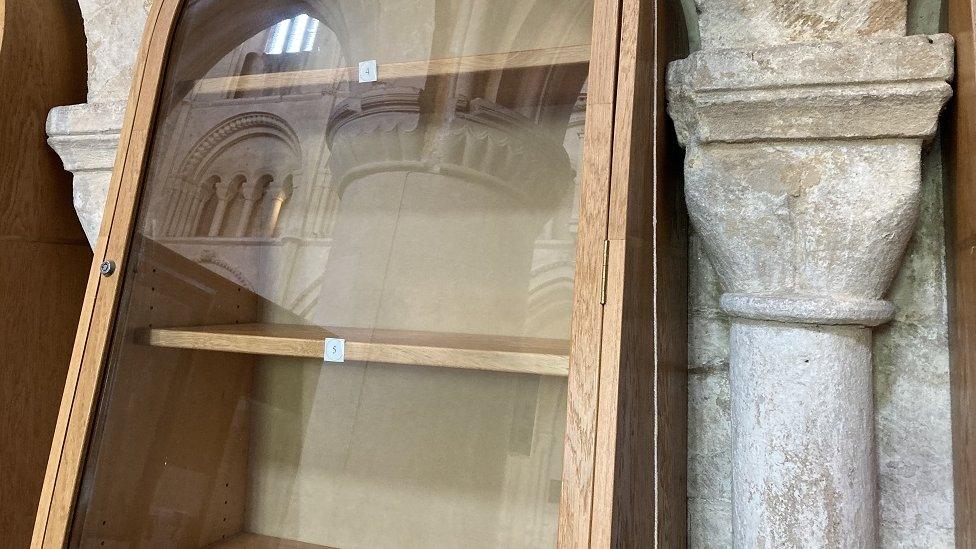 A tall display cabinet with empty shelves next to a medieval stone pillar.