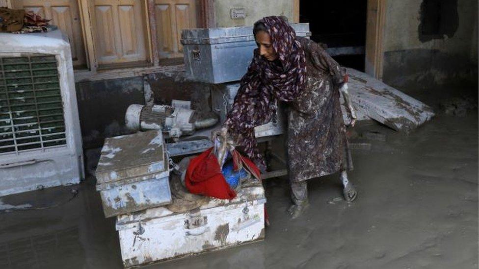 A woman goes through her belongings as she clear her house, following rains and floods during the monsoon season in Nowshera, Pakistan