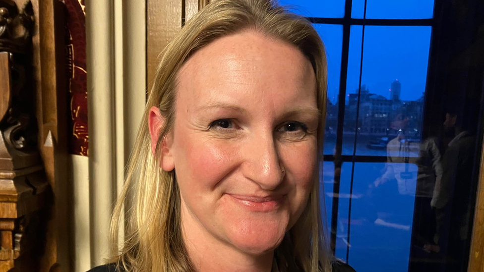 Dr Jess Garland in the Houses of Parliament with a window behind her with a view onto the River Thames