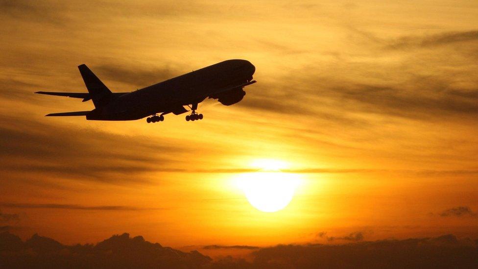 A plane flies past a sunset