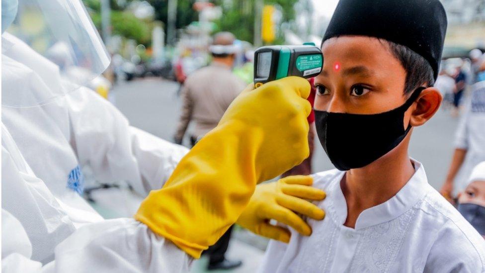 A boy wearing a face mask has his temperature checked before attending Eid prayers