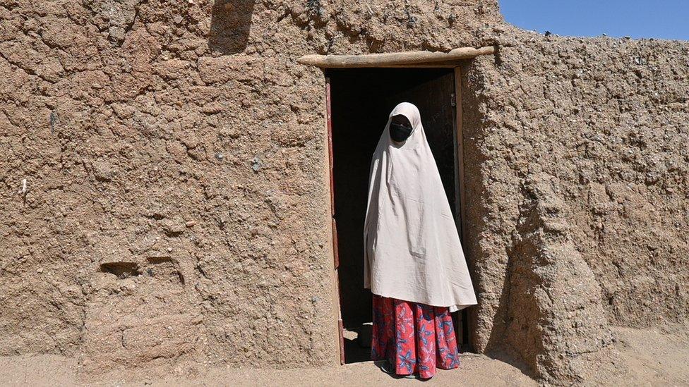 A woman in hijab standing between a door post