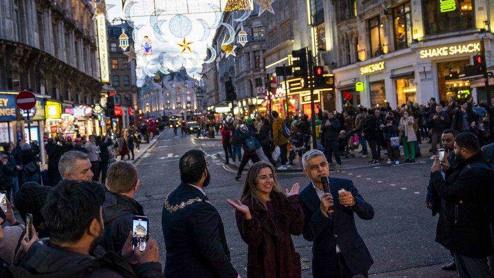 Mayor of London Sadiq Khan speaks into a microphone as people look on