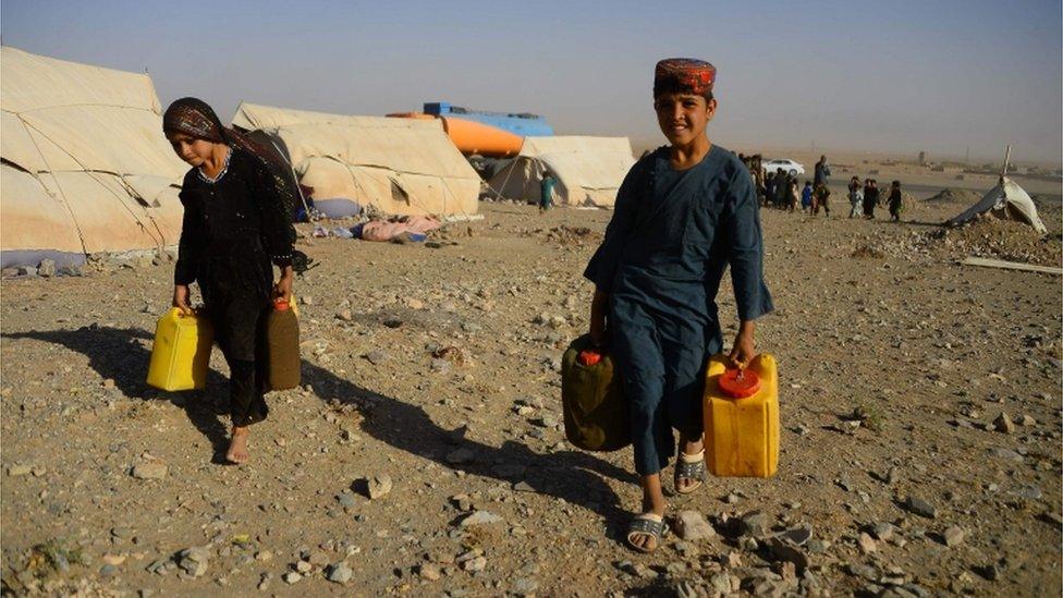 In this photo taken on August 3, 2018, drought-displaced Afghan children carry water containers filled from a tanker at a camp for internally displaced people in Injil district of Herat province